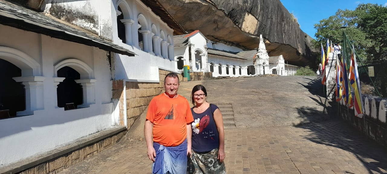 Two guests on the terrace below the Dambulla Cave Temple, with prayer flags on the right